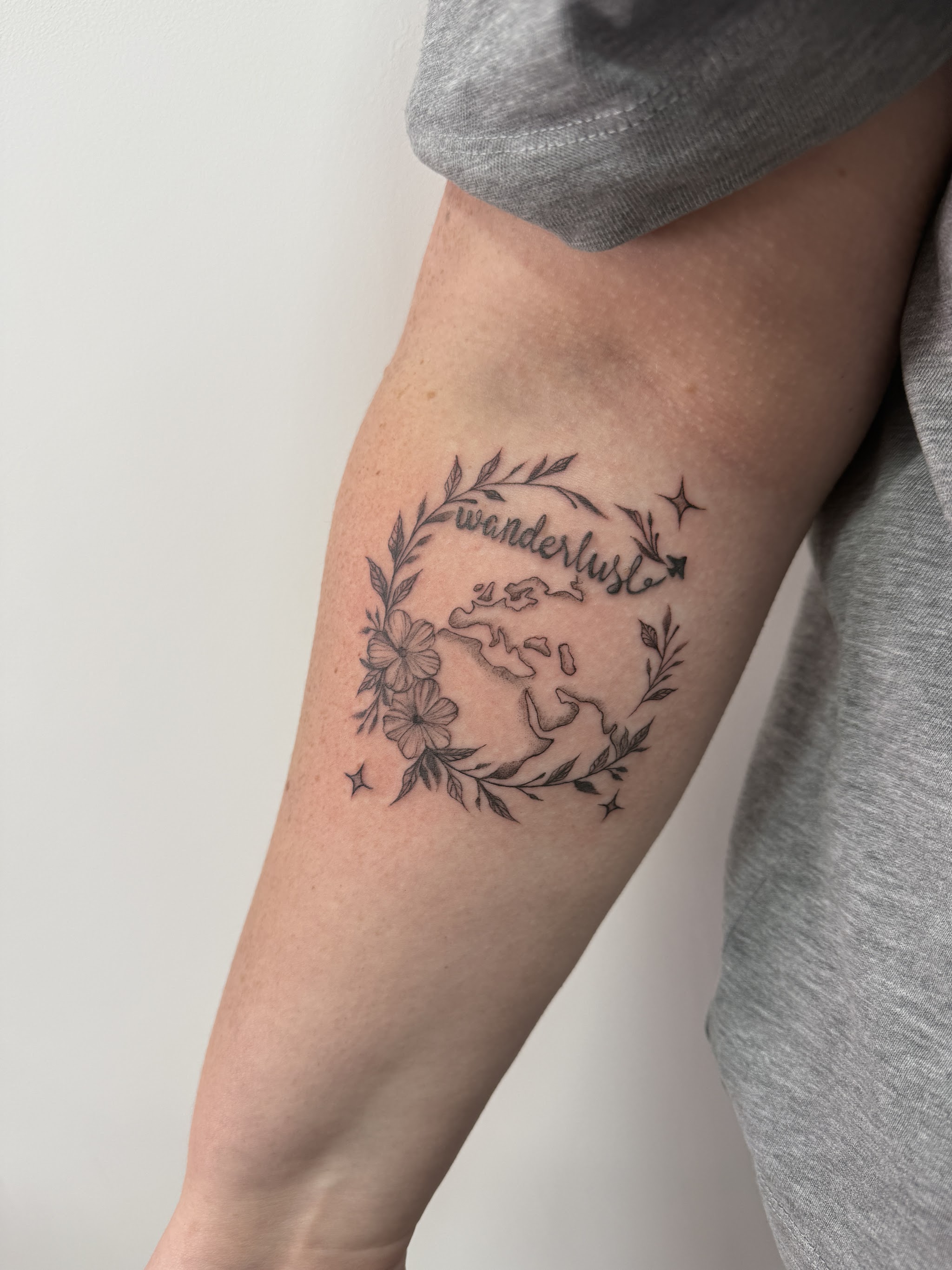 Fine line floral wreath tattoo with script on a forearm